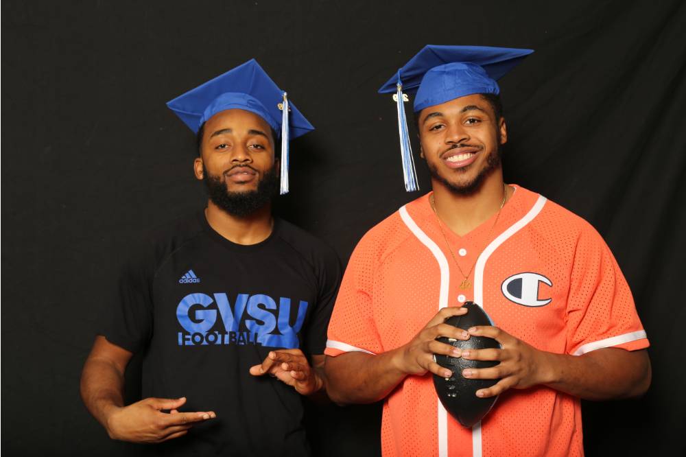 two graduates with one holding a football